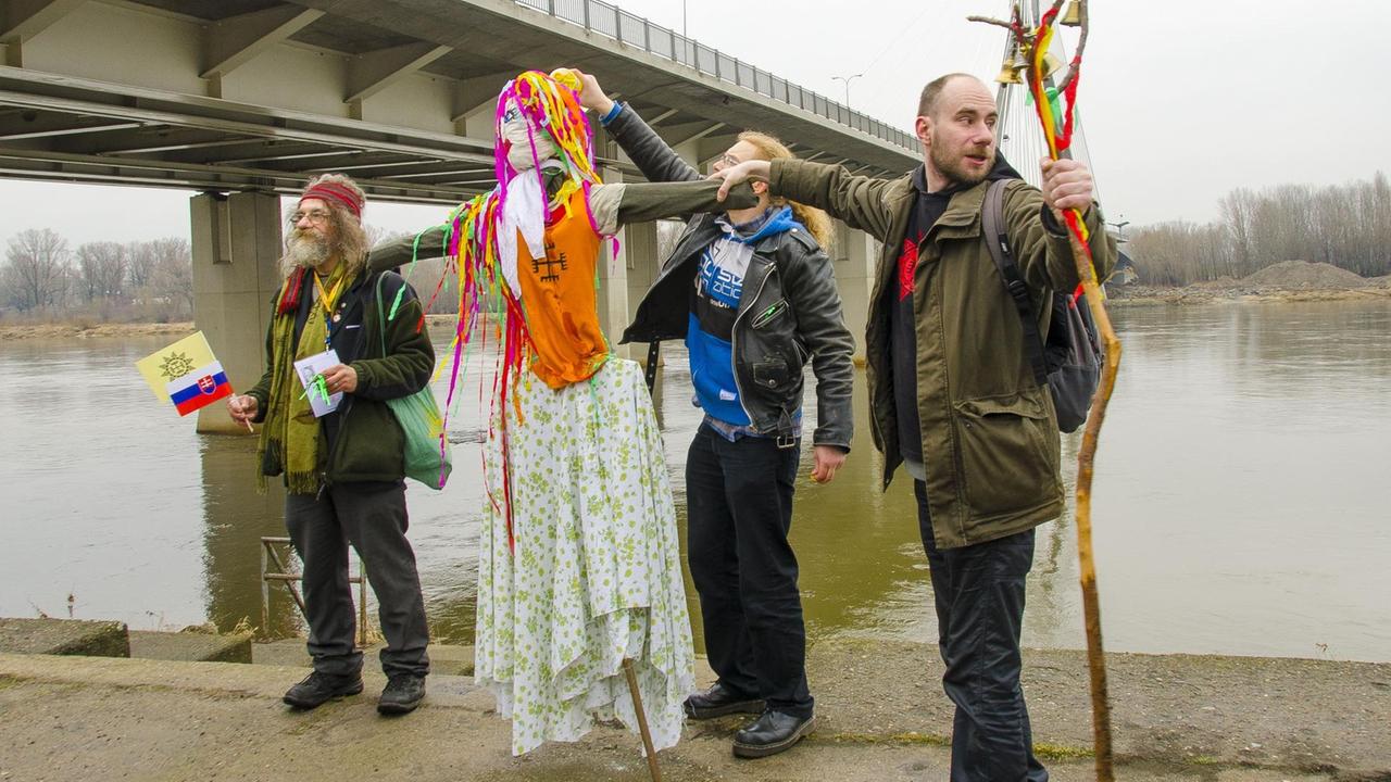 Menschengruppe steht mit einer Strohpuppe am Flussufer Menschengruppe steht mit einer Strohpuppe am Flussufer