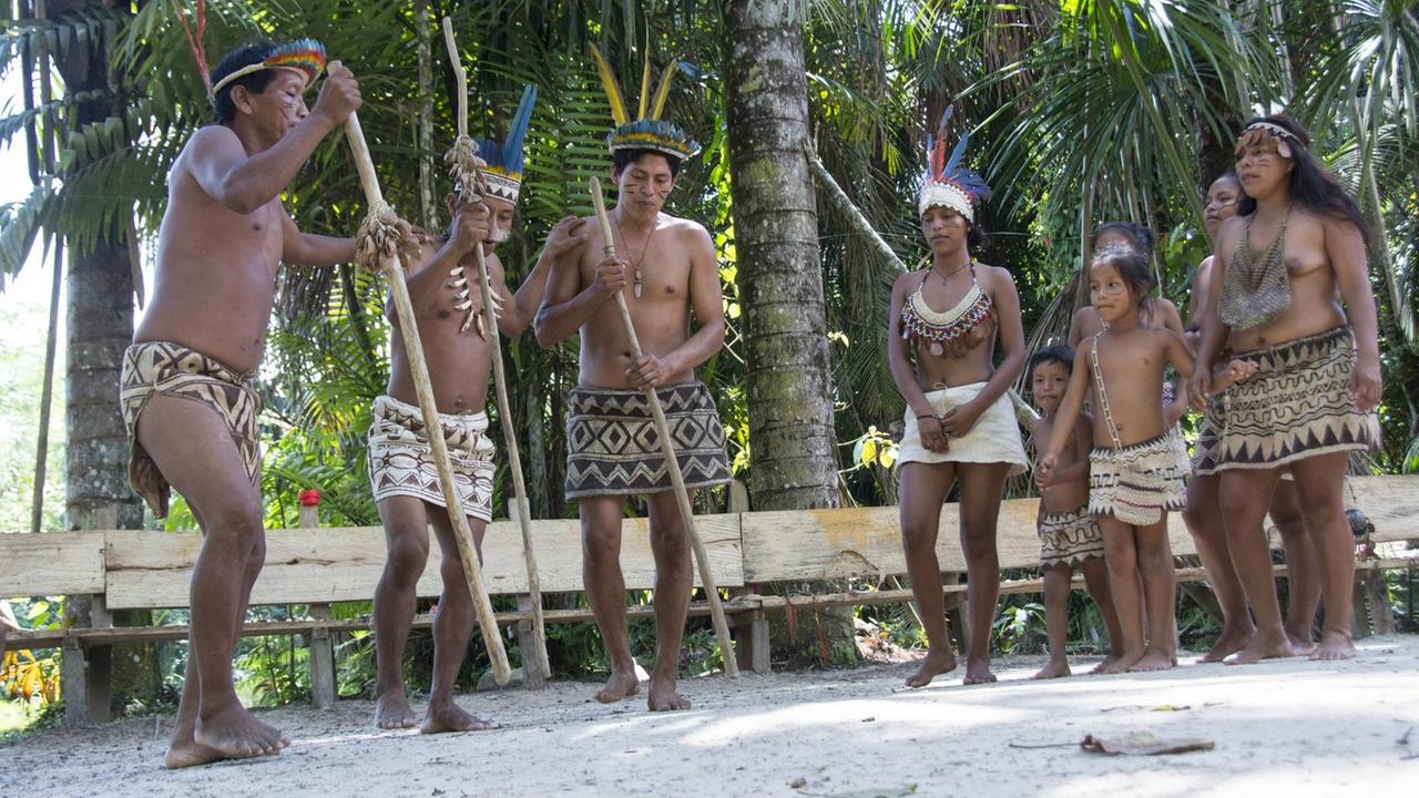 Eine Gruppe von Bora-Indianern steht auf einem sandigen Platz. Die Männer haben lange Holzstäbe in der Hand, während die Frauen und Kinder ihnen zuschauen. Eine Gruppe von Bora-Indianern steht auf einem sandigen Platz. Die Männer haben lange Holzstäbe in der Hand, während die Frauen und Kinder ihnen zuschauen.