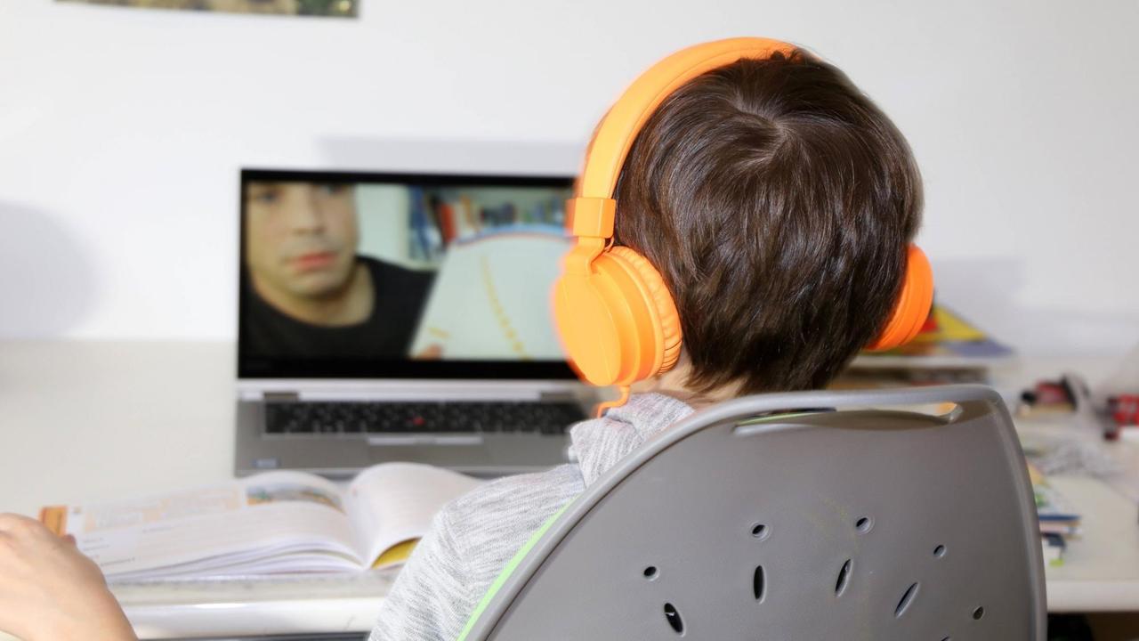 Ein junge mit orangenen Kopfhörern sitzt mit Schulbüchern vor einem Computer.