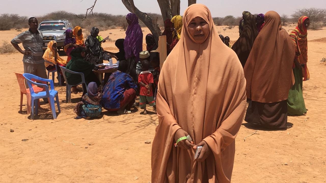 Zu sehen ist Krankenschwester Maryan Mahamed Nuur vor einem Baum, an dem sich Frauen versammeln. Zu sehen ist Krankenschwester Maryan Mahamed Nuur vor einem Baum, an dem sich Frauen versammeln.