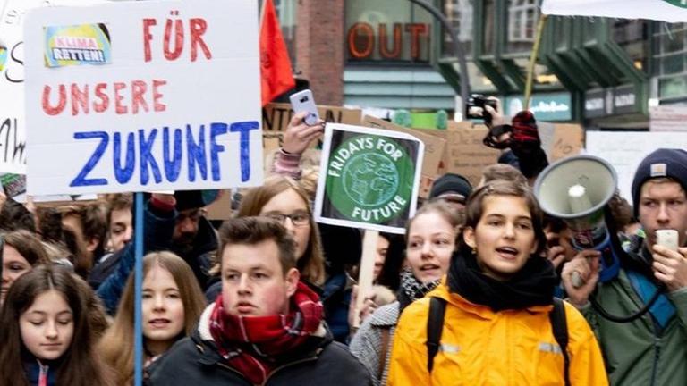 Zahlreiche Demonstrantinnen und Demonstranten gehen durch die Straßen und halten ein Transparent vor sich. Zahlreiche Demonstrantinnen und Demonstranten gehen durch die Straßen und halten ein Transparent vor sich.