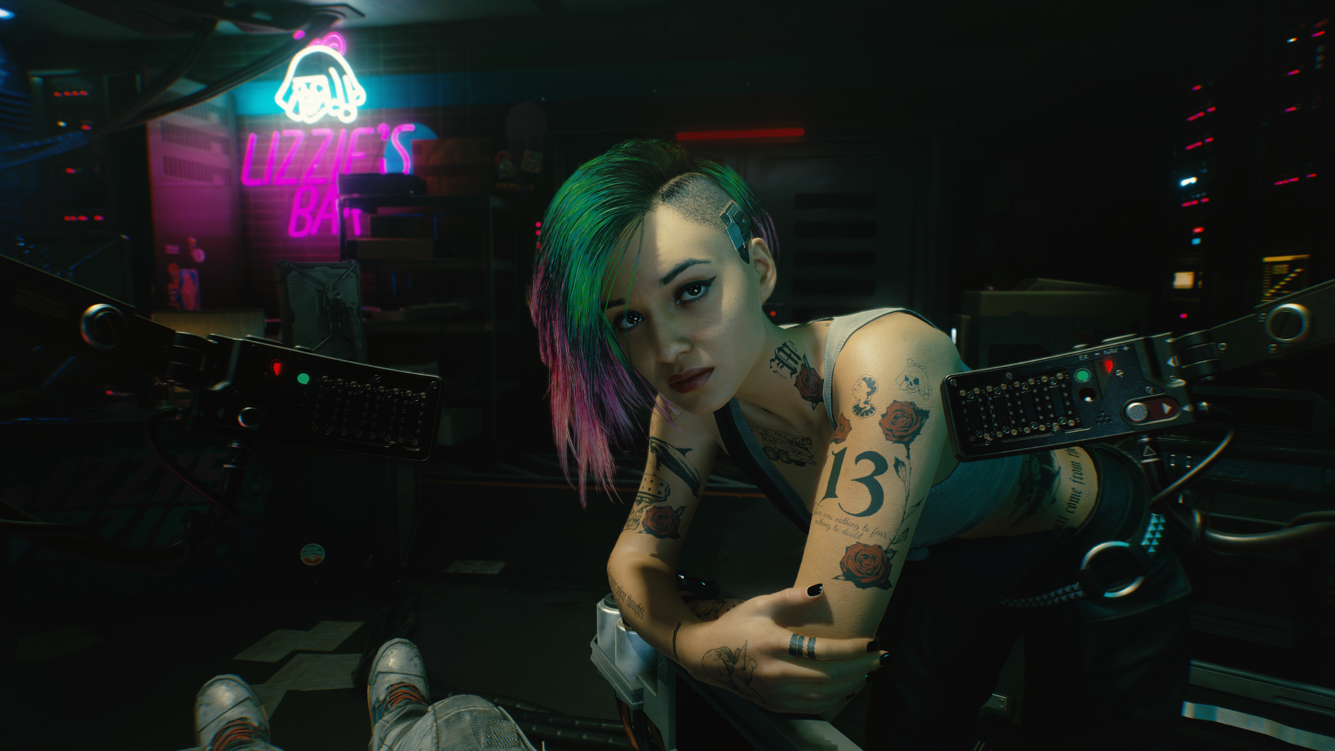 Screenshot aus dem Rollenspiel "Cyberpunk 2077:Eine junge Frau mit vielen Tattoos und bunten, auf einer Seite abrasierten Haaren beugt sich zum Betrachter und blickt ihn ernst an. Hinter ihr befindet sich der Neon-Schriftzug "Lizzie's Bar" Screenshot aus dem Rollenspiel "Cyberpunk 2077:Eine junge Frau mit vielen Tattoos und bunten, auf einer Seite abrasierten Haaren beugt sich zum Betrachter und blickt ihn ernst an. Hinter ihr befindet sich der Neon-Schriftzug "Lizzie's Bar"