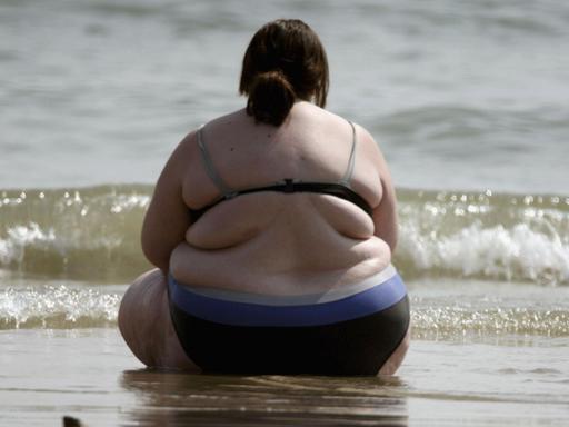 Eine dicke Frau sitzt am Strand.