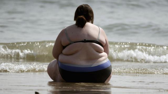 Eine dicke Frau sitzt am Strand.