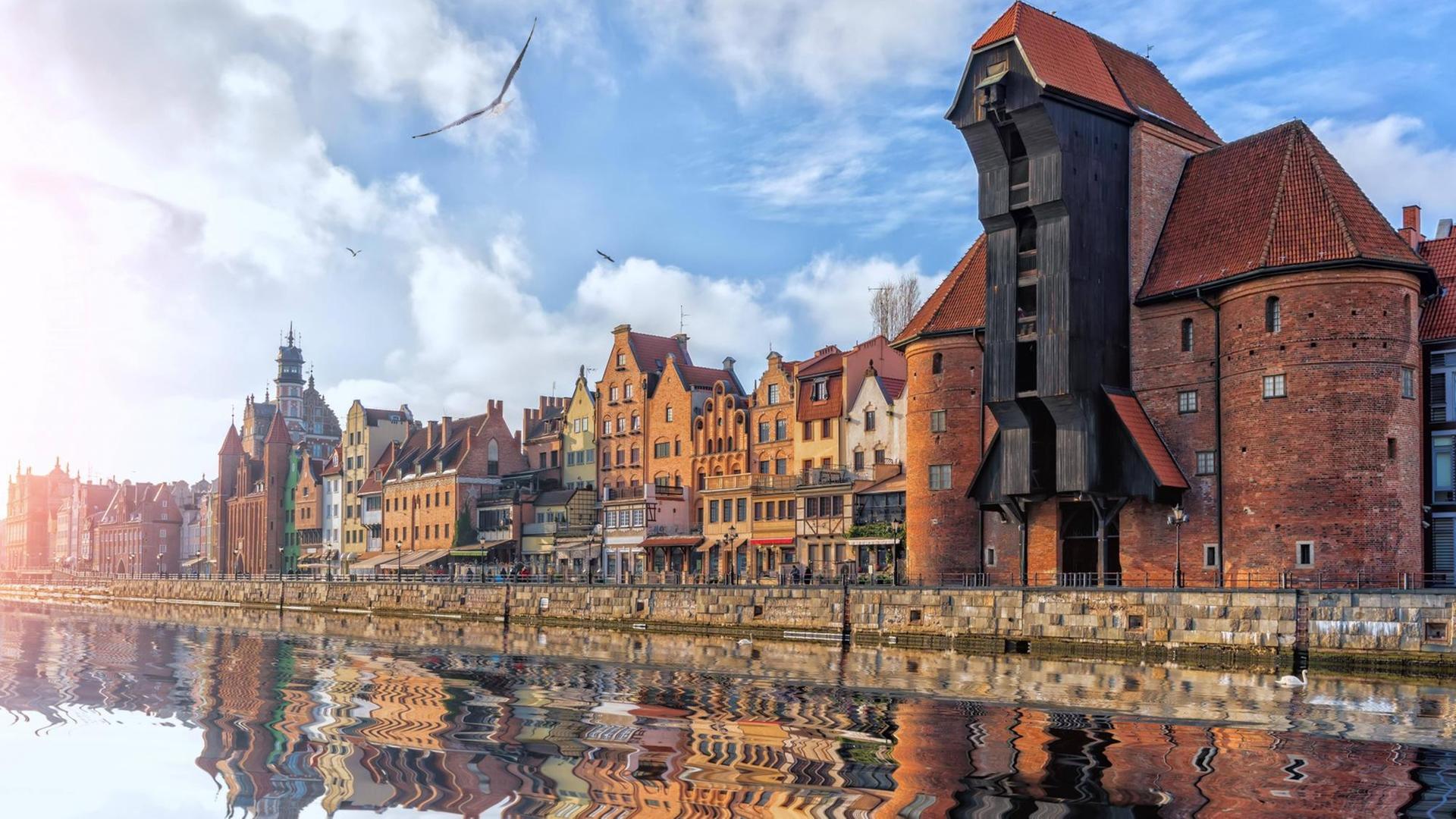 Blick auf das Hafengelände mit historischem Kran und alten Häusern, die sich allesam im Wasser spiegeln. Blick auf das Hafengelände mit historischem Kran und alten Häusern, die sich allesam im Wasser spiegeln.