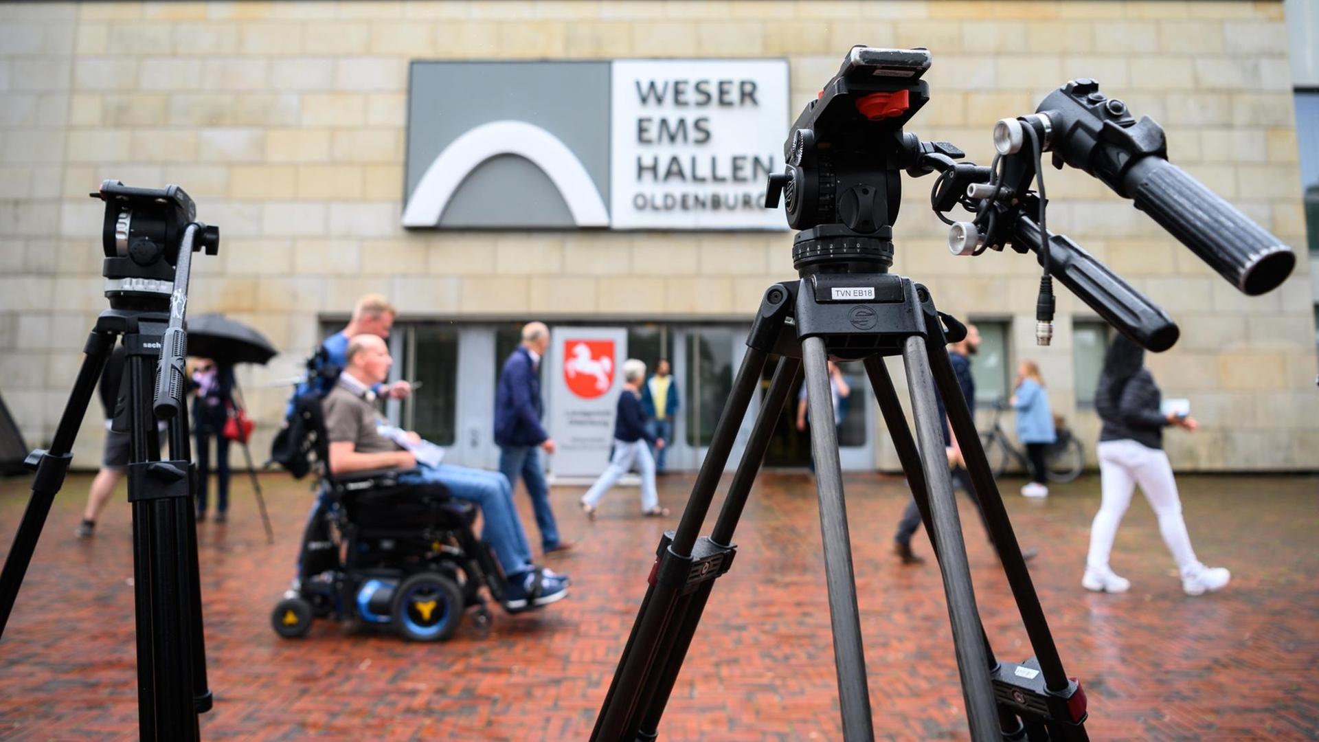 Personen sind während des letzten Prozesstages des Patientenmörders Niels Högel vor der Weser-Ems-Halle hinter zwei Filmstativen. Personen sind während des letzten Prozesstages des Patientenmörders Niels Högel vor der Weser-Ems-Halle hinter zwei Filmstativen.