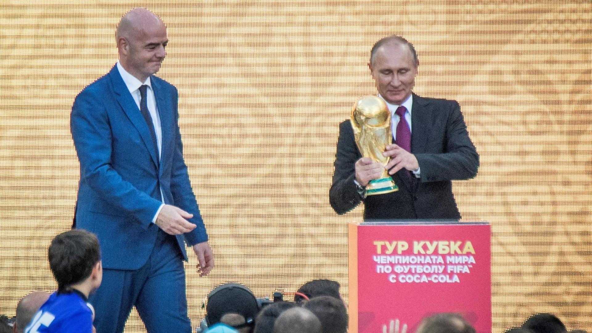 Die Fußball-WM 2018 war in Russland. Im Bild ist der FIFA-Chef Gianni Infantino. Russlands Präsident Wladimir Putin hält den WM-Pokal.