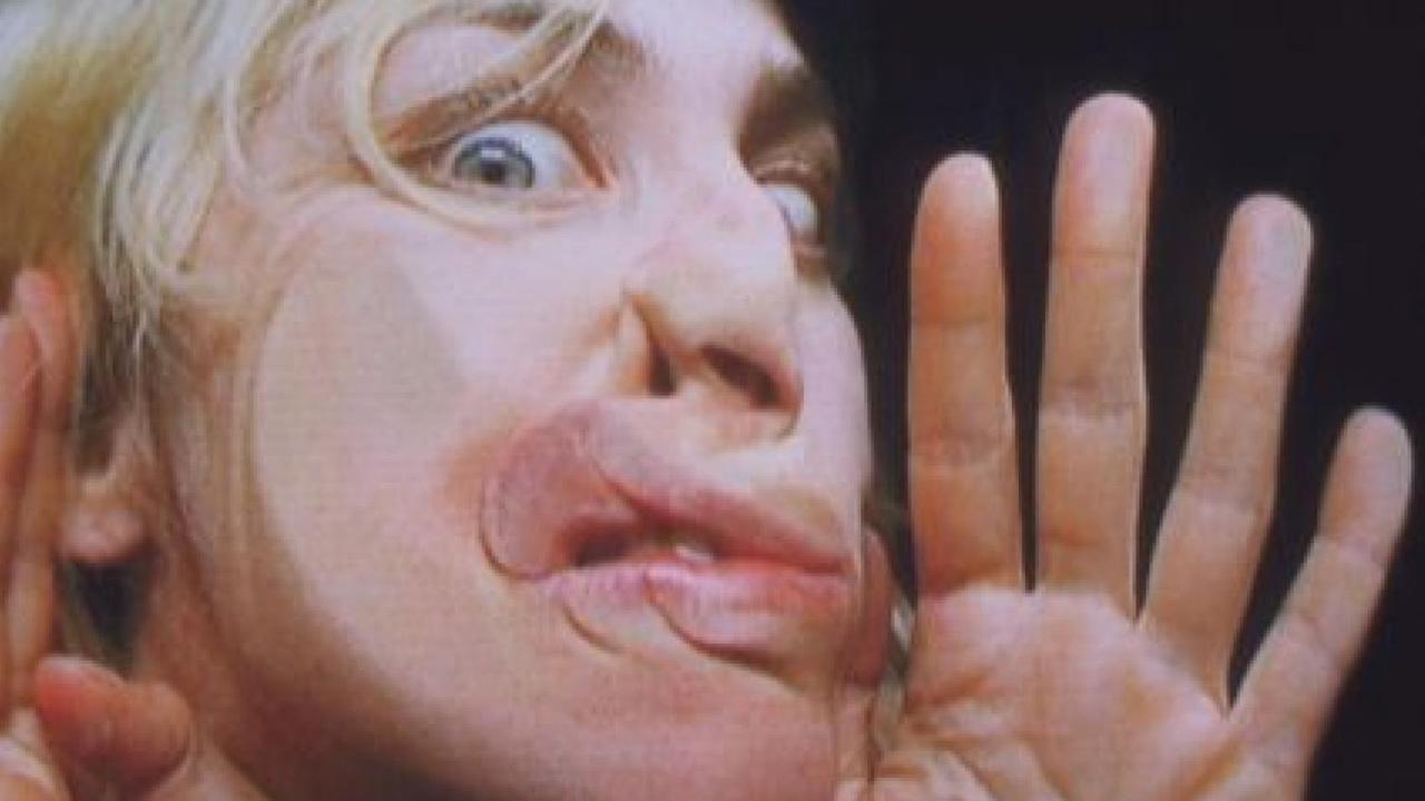 Eine blonde Frau mit blauen Augen presst ihr Gesicht gegen eine unsichtbare Scheibe. Ihre Nase und Mund sind plattgedrückt, ihre Augen weit aufgerissen.