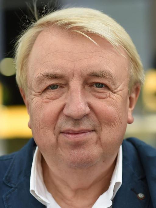 Hanns-Josef Ortheil hat blonde Haar und trägt ein weißes Hemd und dunkle Jacke. Er blickt in Richtung Kamera