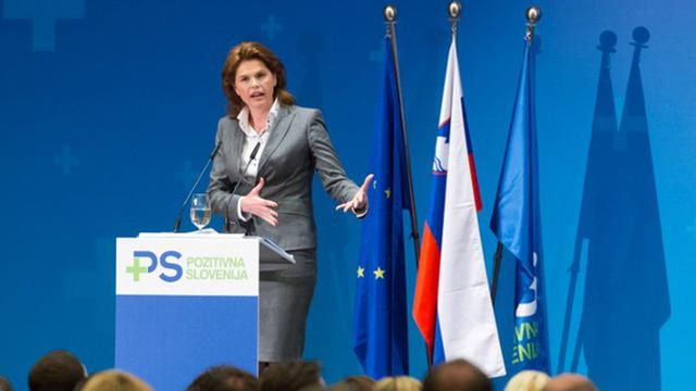 Alenka Bratusek steht auf einer Bühne hinter einem Rednerpult und gestikuliert. Dahinter sind die Flaggen der EU, Sloweniens und der Partei "Positives Slowenien" zu sehen.