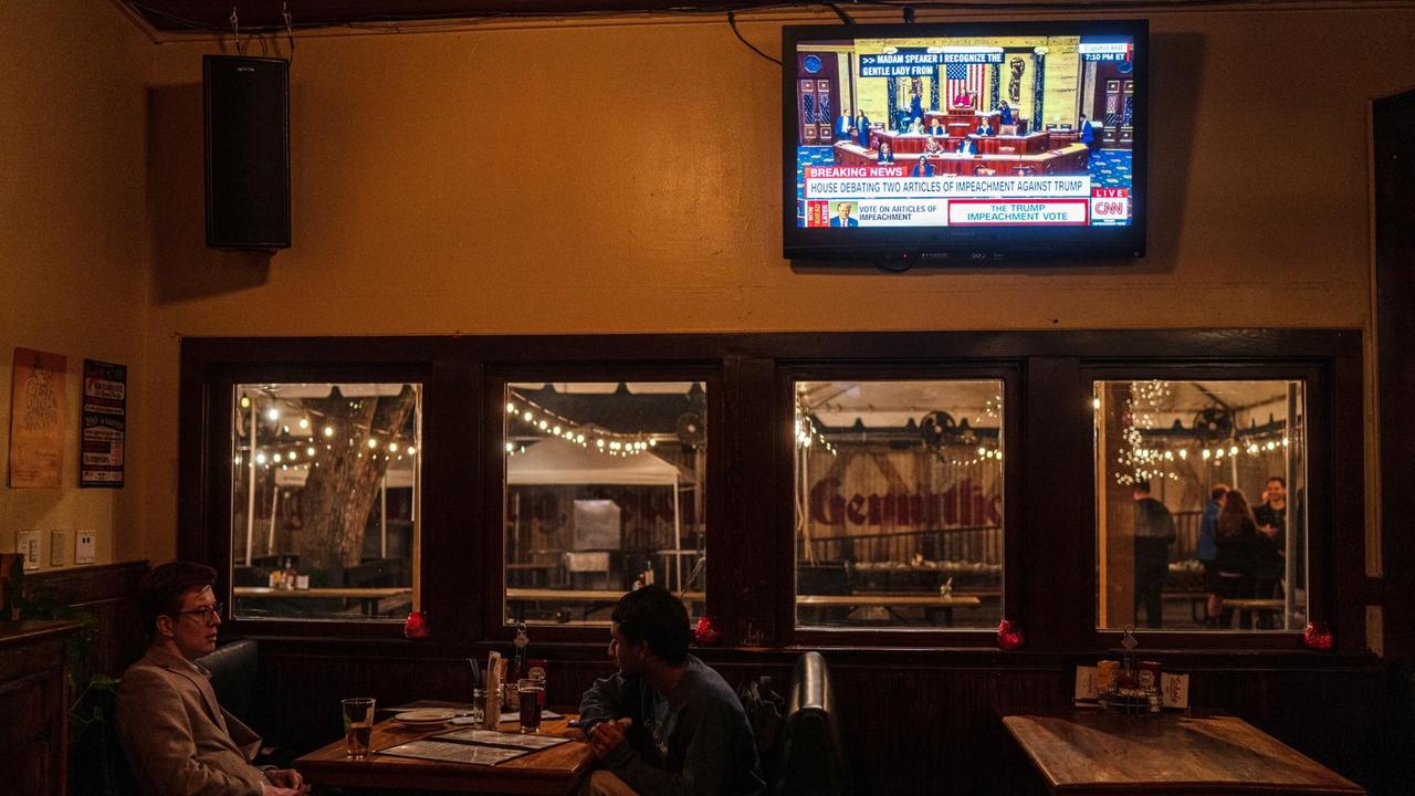 Zwei Männer sitzen in einer Bar unter einem laufenden Fernseher. Zwei Männer sitzen in einer Bar unter einem laufenden Fernseher.