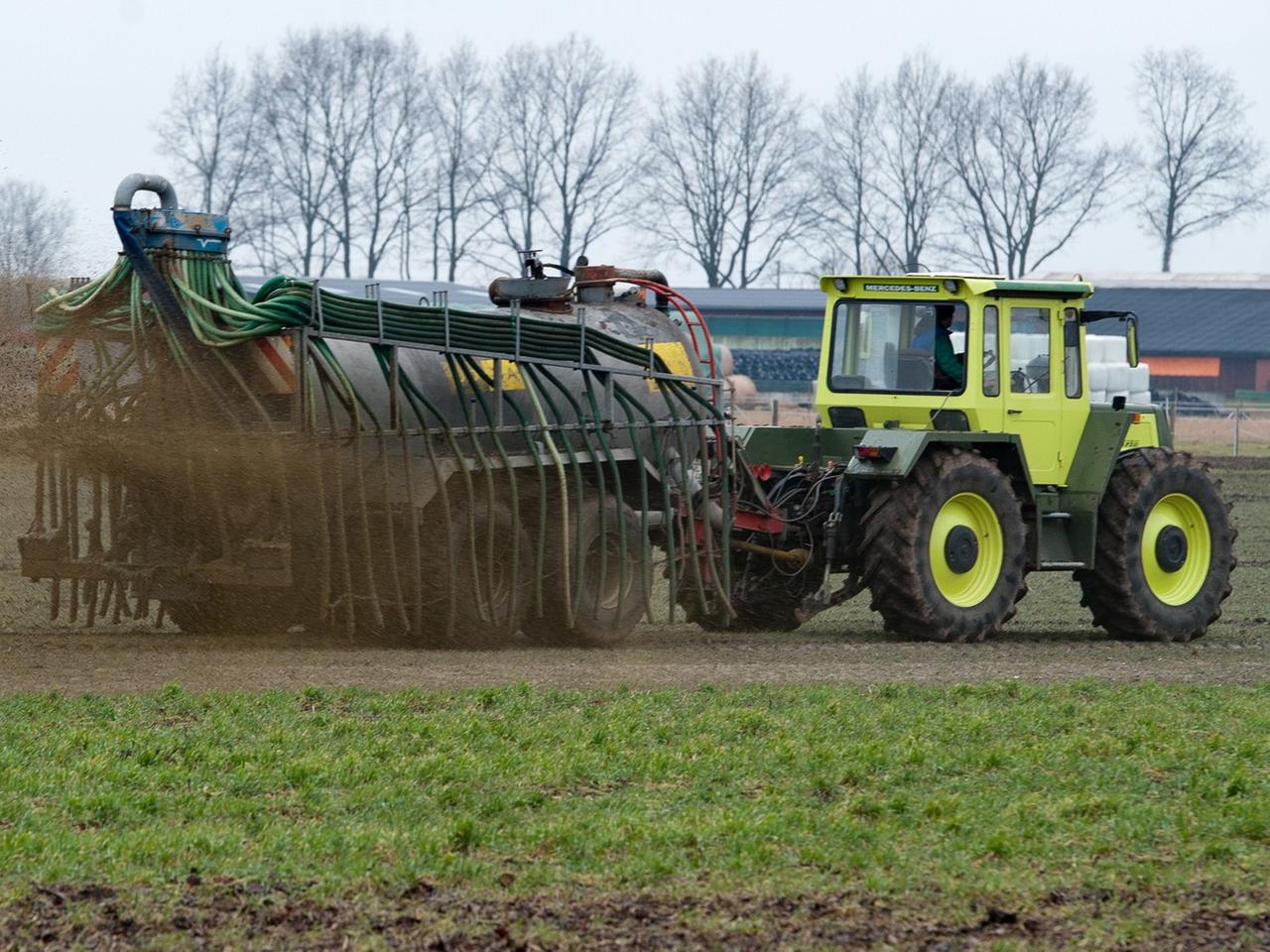 Ein gelber Traktor mit Anhänger, aus dem braue Gülle auf ein Feld gespritzt wird. Ein gelber Traktor mit Anhänger, aus dem braue Gülle auf ein Feld gespritzt wird.