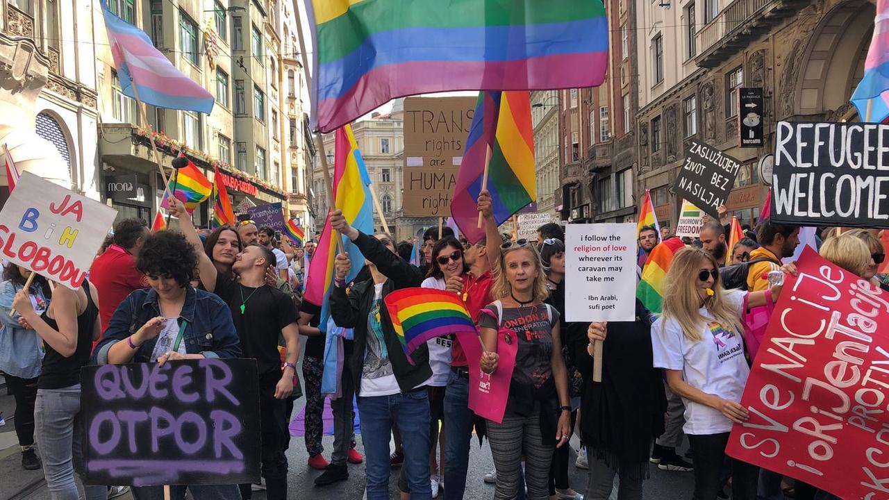 Die erste Pride Parade für die Rechte von LGBTQ-Menschen in den Straßen Sarajewos. Zu sehen sind Männer und Frauen, die Regenbogenfahnen schwenken und Transparente hochhalten.