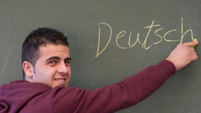 Asylbewerber Hamza Rezgar aus Syrien schreibt in der Städtischen Berufsschule II in Regensburg (Bayern) das Wort "Deutsch" an die Tafel.