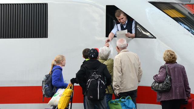 Reisende am Bahnsteig des Hauptbahnhofs in München reden mit einem Lokführer der Deutschen Bahn, der aus dem Fenster eines ICE schaut.