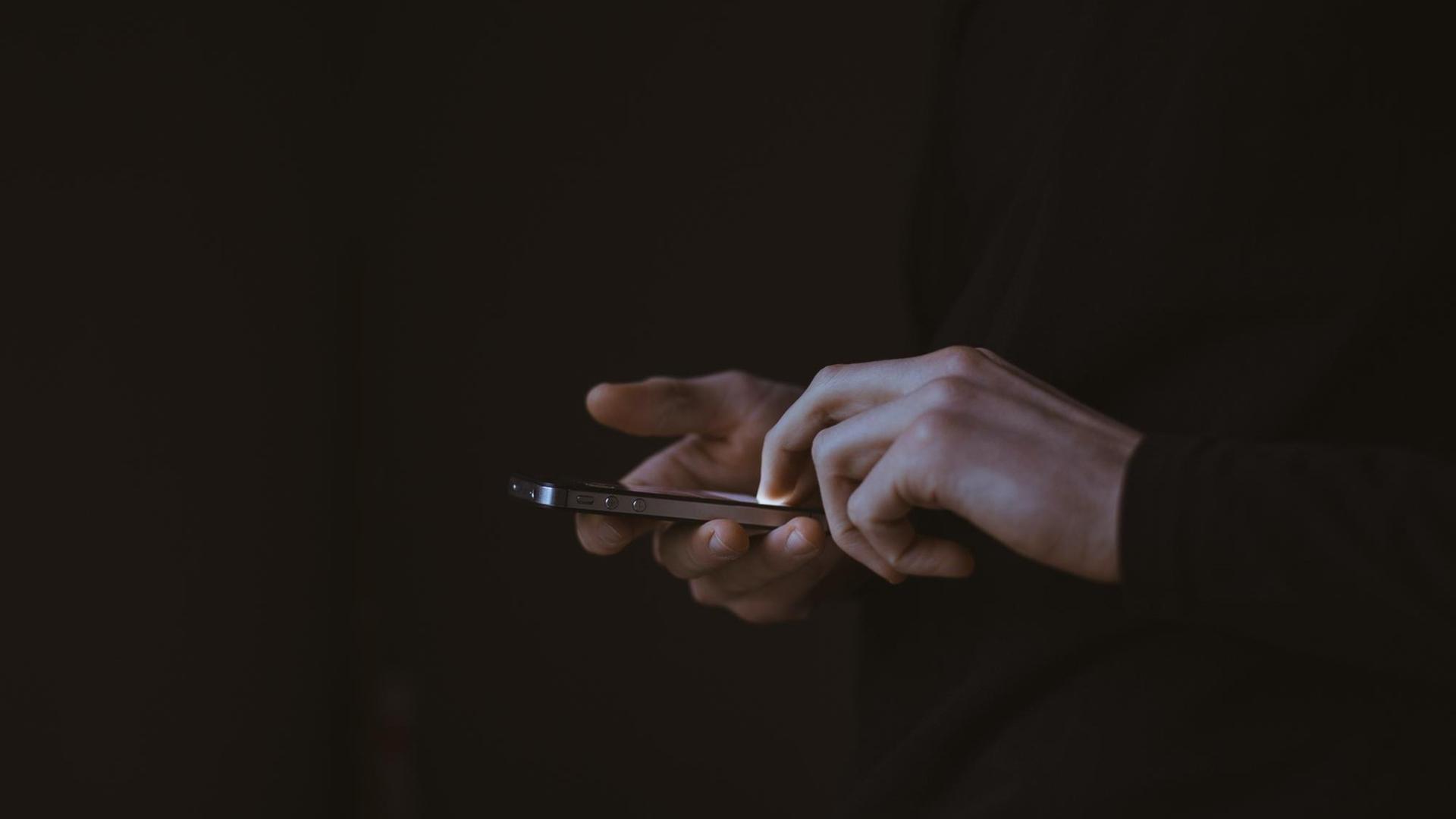 Eine Person hält im Dunklen ein Smartphone in der Hand, das Display leuchtet. Eine Person hält im Dunklen ein Smartphone in der Hand, das Display leuchtet.