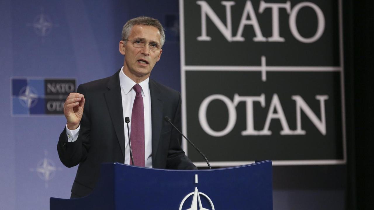 Stoltenberg spricht und gestikuliert an einem Rednerpult mit der NATO-Windrose. Hinter ihm der Schriftzug NATO/OTAN.