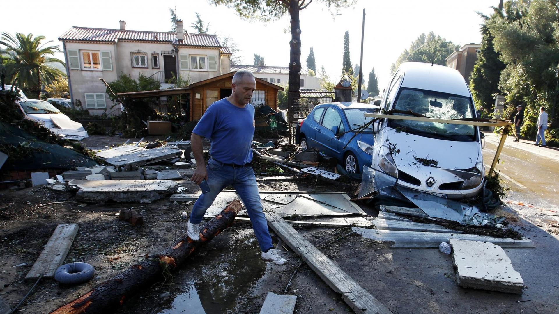 Ein Mann läuft über Trümmerteile und an zerstörten Autos vorbei.