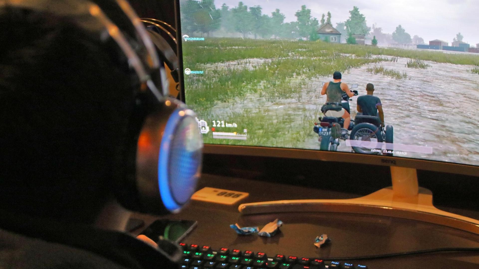 Ein junger Mann sitzt vor einem Bildschrim. Er trägt Kopfhörer und spielt "PlayerUnknown's Battlegrounds" Ein junger Mann sitzt vor einem Bildschrim. Er trägt Kopfhörer und spielt "PlayerUnknown's Battlegrounds"