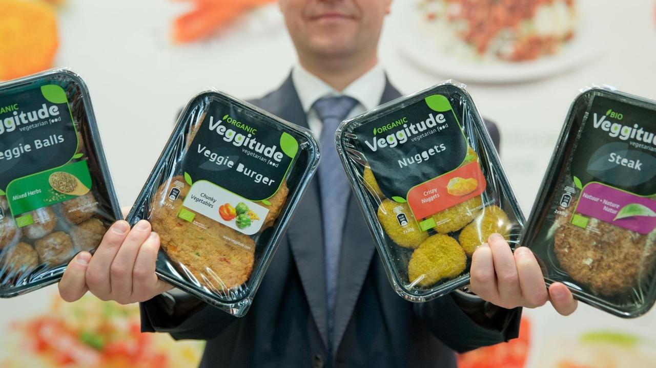 Ein Mann hält verschiedene vegetarische Fleischersatzprodukte nach oben. Ein Mann hält verschiedene vegetarische Fleischersatzprodukte nach oben.