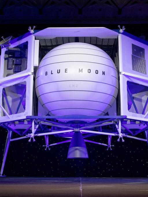 Amazon-Gründer Jeff Bezos steht auf ener Bühne und präsentiert hinter ihm eine in hellem lila angestrahlte Mondlandefähre.