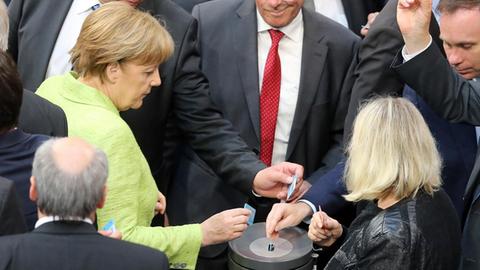 Merkel und andere Abgeordnete stehen mit ihren Abstimmungskärtchen an der Wahlurne.