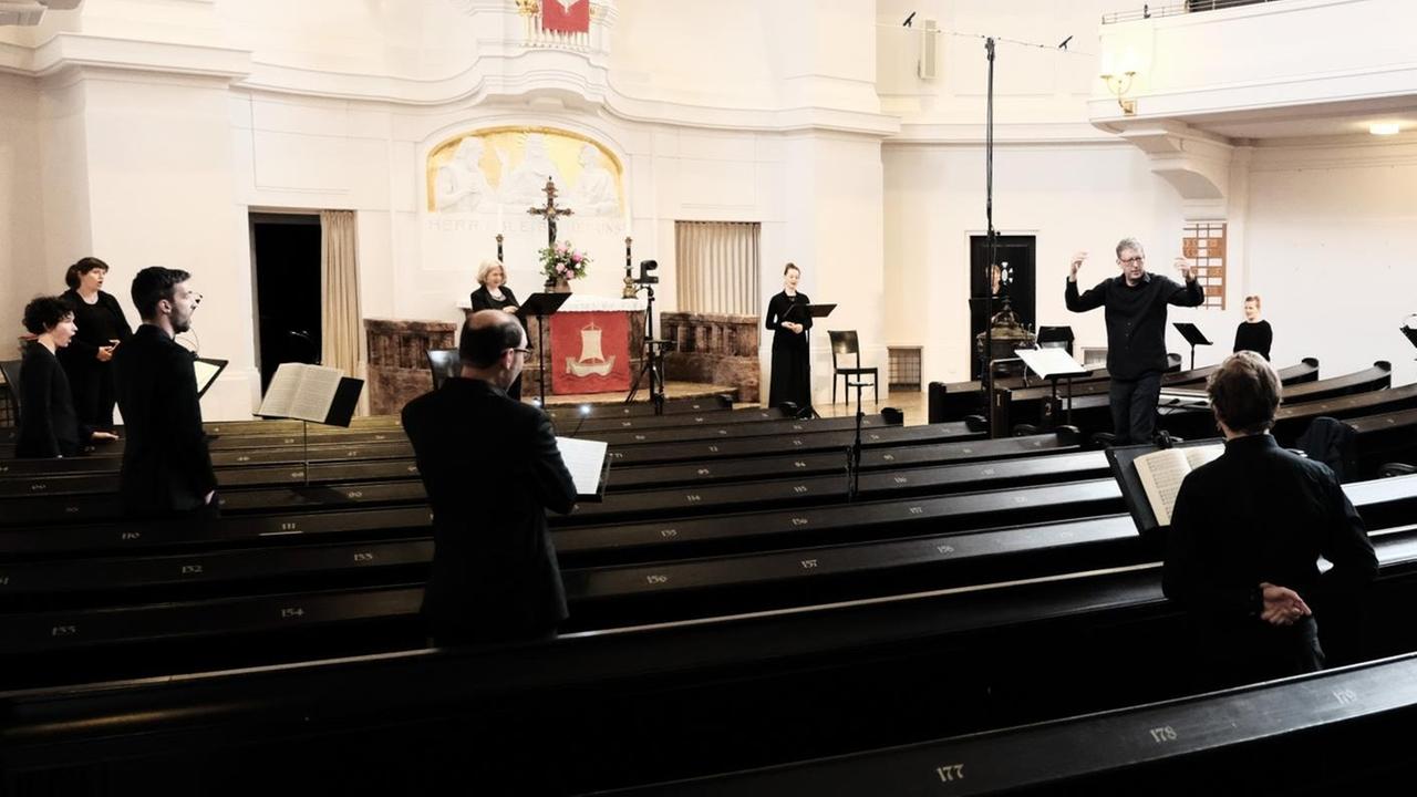 Einige Menschen stehen in den leeren, dunklen Bänken einer Kirche, ihrem Dirigenten zugewandt. Einige Menschen stehen in den leeren, dunklen Bänken einer Kirche, ihrem Dirigenten zugewandt.