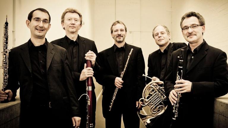 Fünf Musiker stehen beieinander und halten alle ein Blasinstrument in der Hand. Fünf Musiker stehen beieinander und halten alle ein Blasinstrument in der Hand.