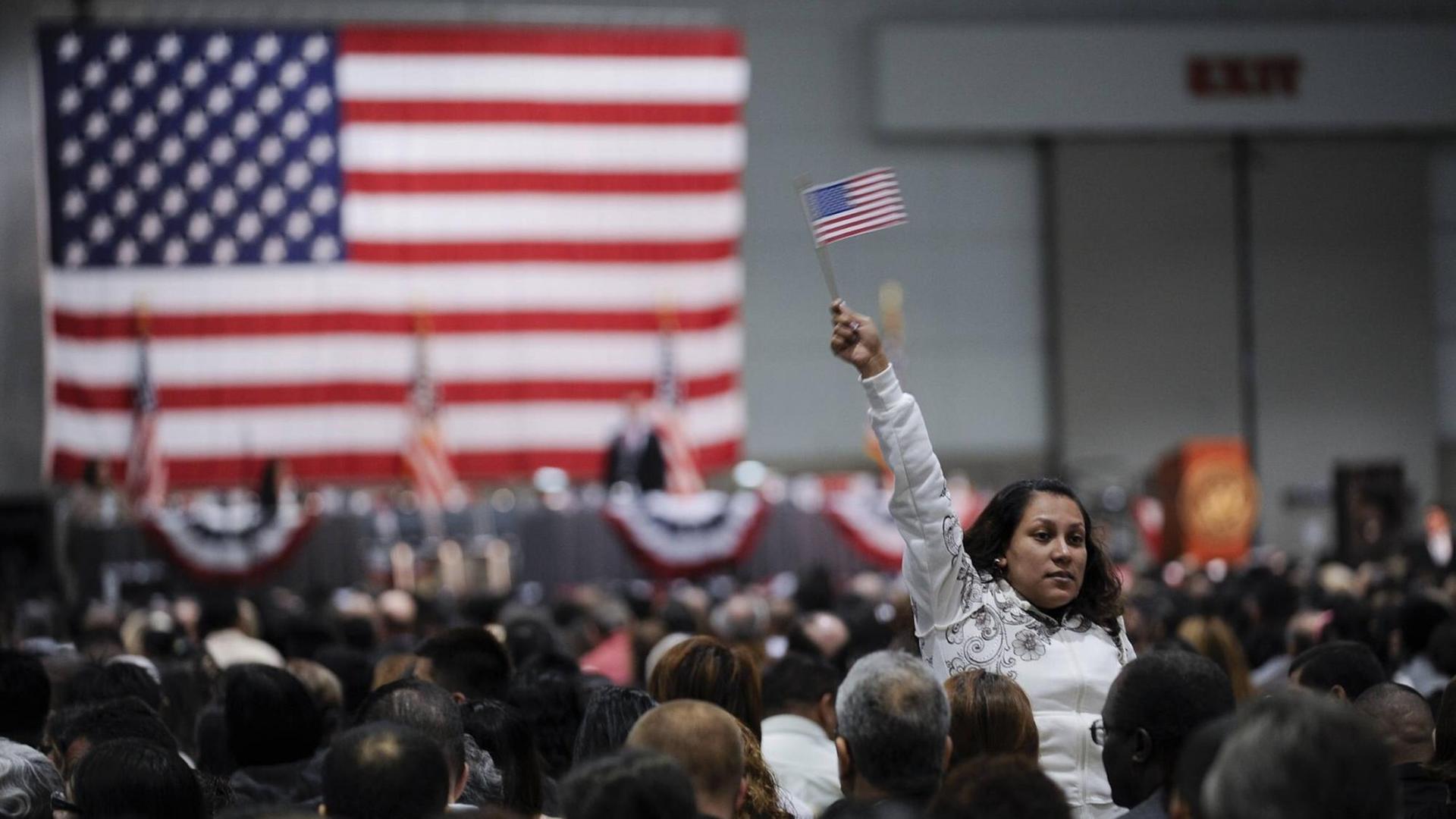 Einwanderer stehen bei einer Einbürgerungszeremonie im Oktober 2010 in Los Angeles vor einer US-Flagge. Der Arm einer Flau ragt aus der Menge. Sie hält eine kleine US-Fahne in der Hand.