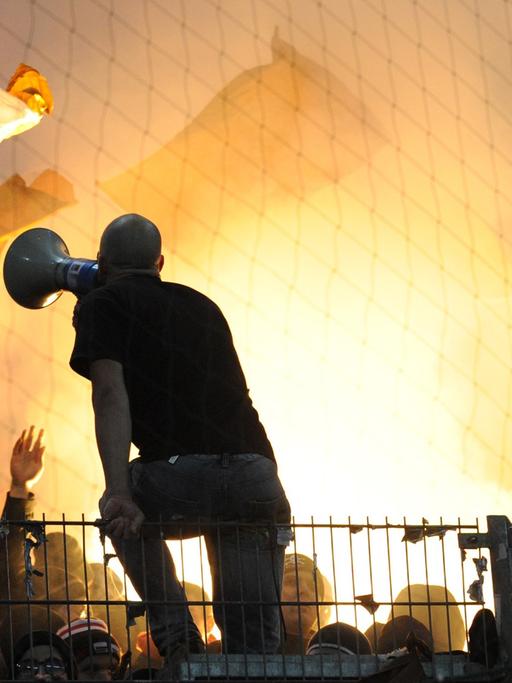 Fans des FC St. Pauli brennen eine Rauchbombe ab, davor ist ein Mann mit Megafon zu sehen.