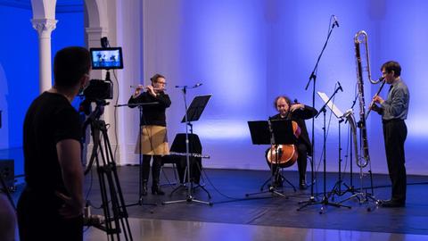 Ein Trio des Ensembles wird von einem Kameramann mit Stativ auf der Bühne gefilmt