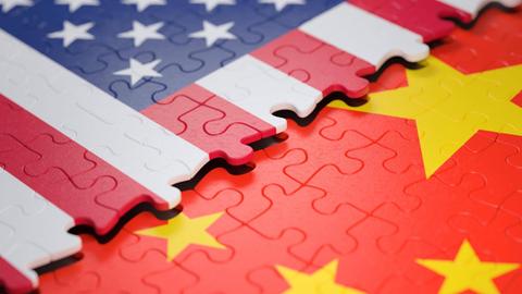Symbolbild: Ein unfertiges Puzzle, das einen Teil der Flagge der USA zeigt, liegt über einem anderen Puzzle, das einen Teil der Flagge Chinas zeigt.