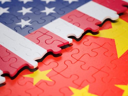 Symbolbild: Ein unfertiges Puzzle, das einen Teil der Flagge der USA zeigt, liegt über einem anderen Puzzle, das einen Teil der Flagge Chinas zeigt.