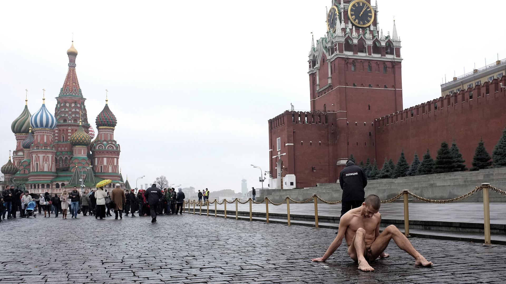 Der russische Aktionskünstler Pjotr Pawlenski sitzt bei der Aktion "Fixierung" nackt auf dem Roten Platz, wo er seinen Hodensack festgenagelt hat. Im Hintergrund die Kremlmauer, die Basilius-Kathedrale, ein Polizist und Touristen. Der russische Aktionskünstler Pjotr Pawlenski sitzt bei der Aktion "Fixierung" nackt auf dem Roten Platz, wo er seinen Hodensack festgenagelt hat. Im Hintergrund die Kremlmauer, die Basilius-Kathedrale, ein Polizist und Touristen.