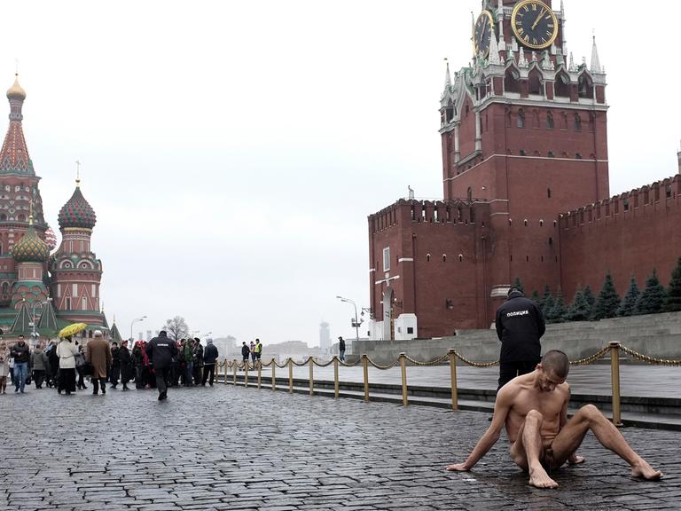 Der russische Aktionskünstler Pjotr Pawlenski sitzt bei der Aktion "Fixierung" nackt auf dem Roten Platz, wo er seinen Hodensack festgenagelt hat. Im Hintergrund die Kremlmauer, die Basilius-Kathedrale, ein Polizist und Touristen.