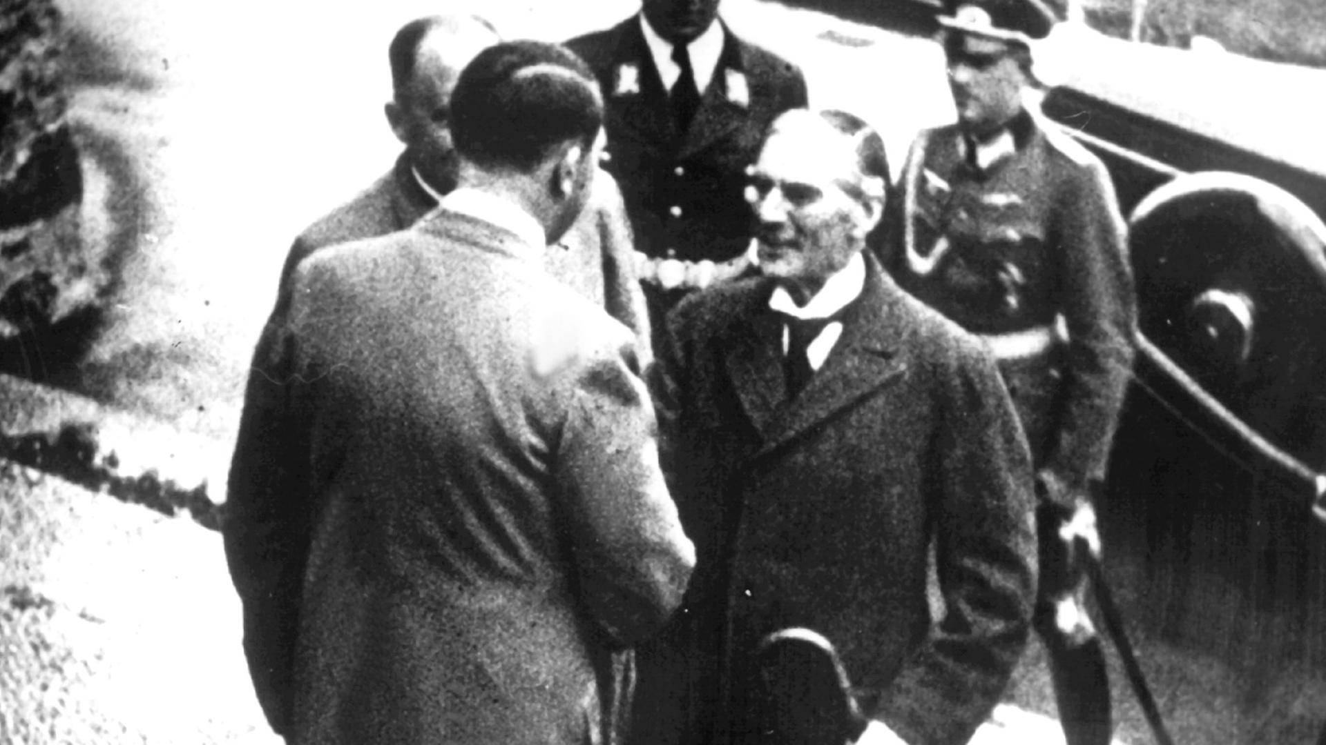 Adolf Hitler, ein paar Stufen über Arthur Neville Chamberlain stehend, schüttelt ihm die Hand