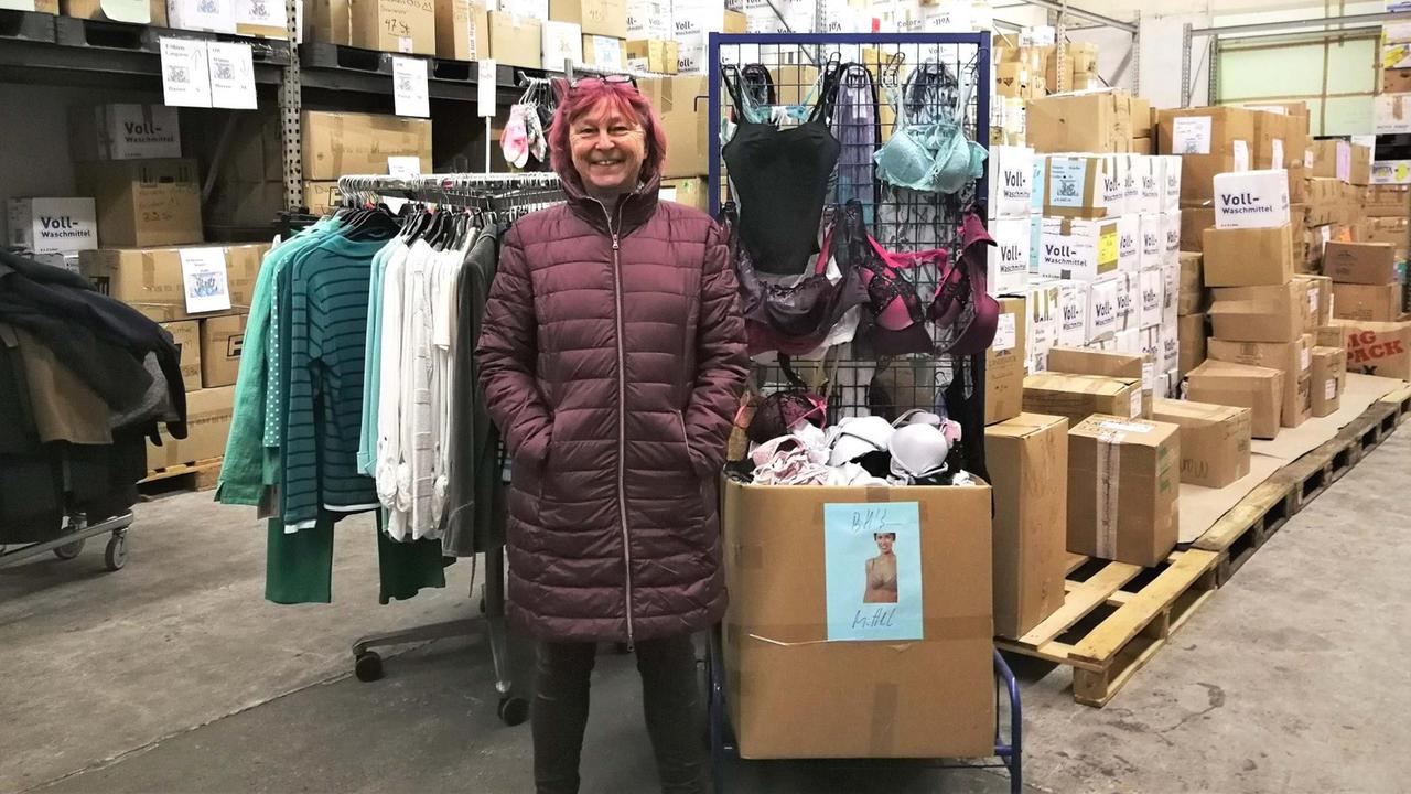 Eine Frau mit dunklen Haaren steht in einem Lagerhaus mit Kleidung und Kisten. Eine Frau mit dunklen Haaren steht in einem Lagerhaus mit Kleidung und Kisten.