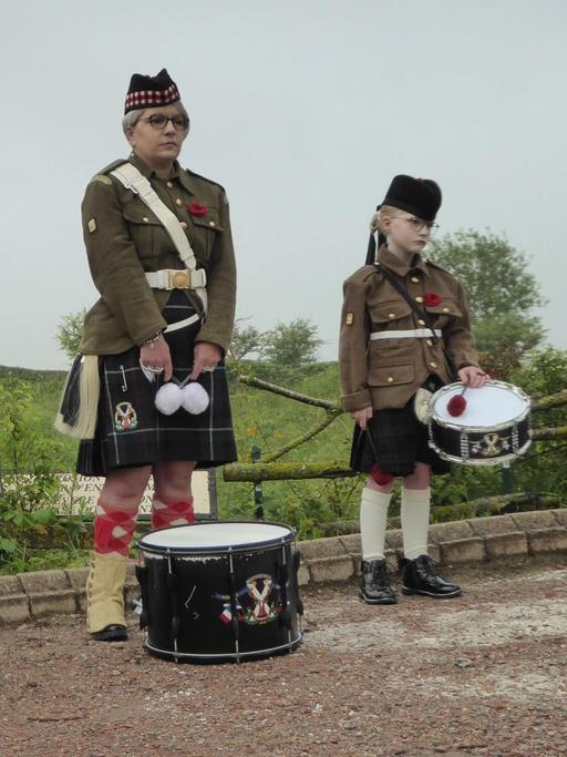 Ein Mann, zwei junge Frauen und ein Mädchen stehen mit Trommeln und schottischer Tracht nebeneinander