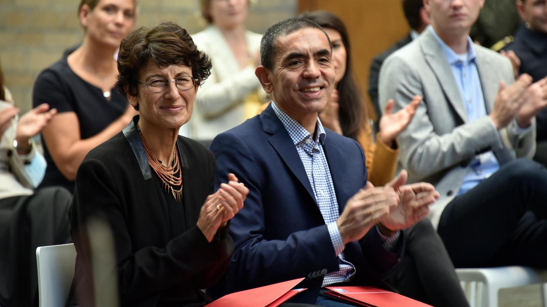 Die Mediziner Ugur Sahin (r) und Özlem Türeci im Rathaus der Stadt Köln. Sie sitzen auf Stühlen im Publikum und applaudieren. Die Mediziner Ugur Sahin (r) und Özlem Türeci im Rathaus der Stadt Köln. Sie sitzen auf Stühlen im Publikum und applaudieren.