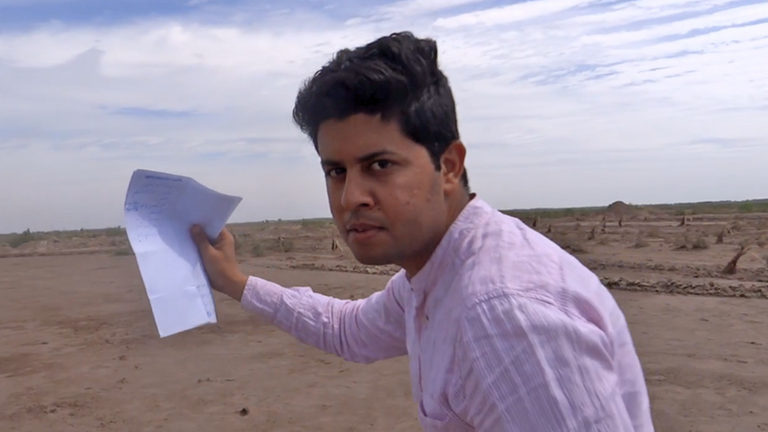Der irakische Lyriker Kadhem Khanjar bei einer Performance in einem Minenfeld: Er hält ein Blatt Papier hoch, auf dem ein Gedicht steht, das er gleich beim Rennen durch das Minenfeld vorlesen wird. Er blickt herausfordernd in die Kamera. Der irakische Lyriker Kadhem Khanjar bei einer Performance in einem Minenfeld: Er hält ein Blatt Papier hoch, auf dem ein Gedicht steht, das er gleich beim Rennen durch das Minenfeld vorlesen wird. Er blickt herausfordernd in die Kamera.