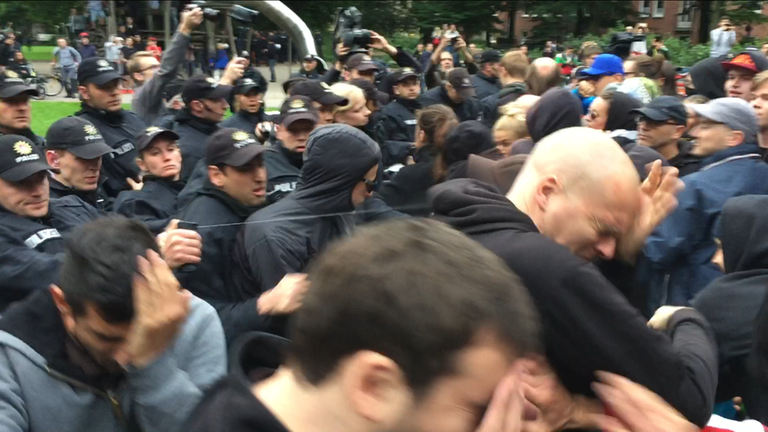 In einer Menschenmenge setzt ein Polizist Reizgas ein, mehrere Menschen halten sich die Hände vors Gesicht In einer Menschenmenge setzt ein Polizist Reizgas ein, mehrere Menschen halten sich die Hände vors Gesicht
