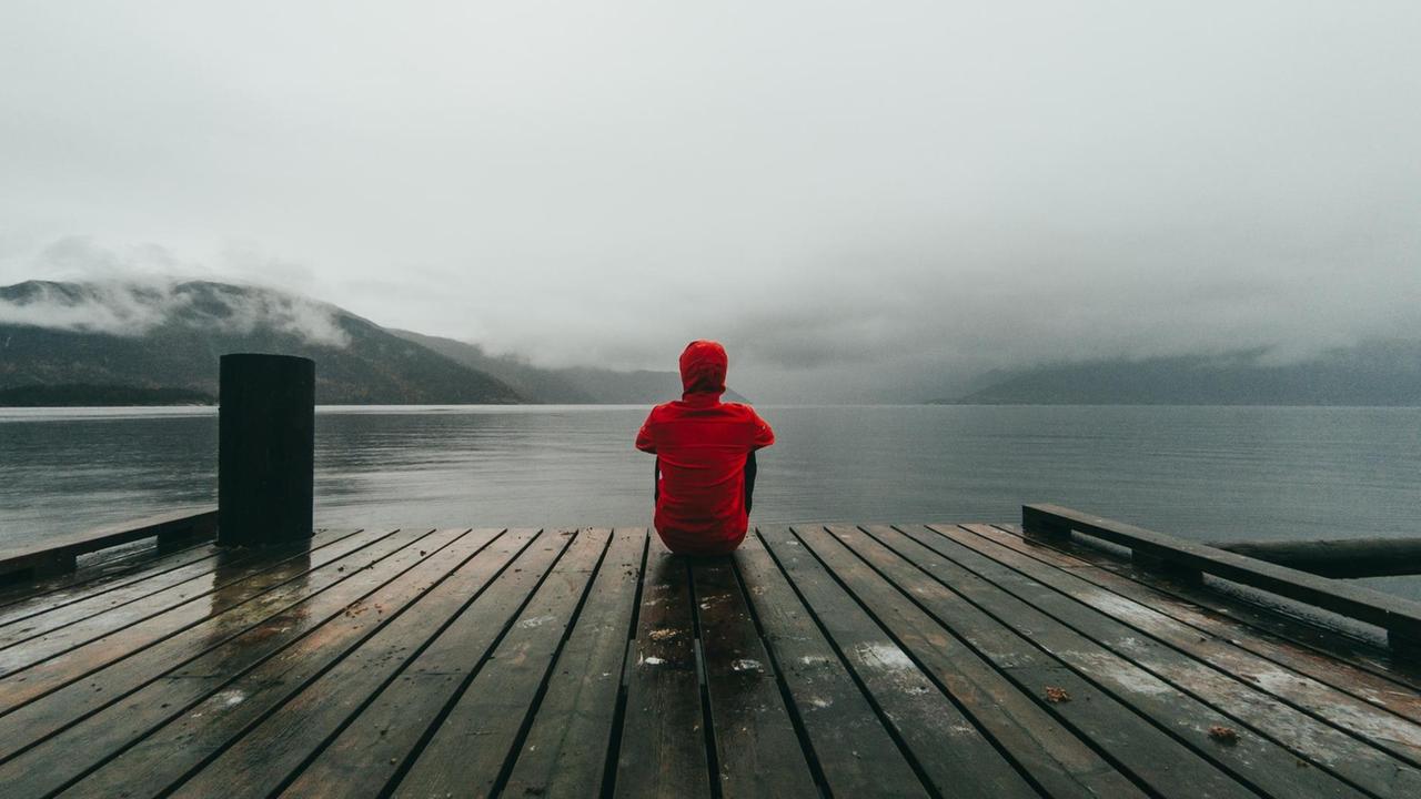 Ein Mann sitzt auf einem Steg eines Sees und blickt auf das Wasser. Ein Mann sitzt auf einem Steg eines Sees und blickt auf das Wasser.