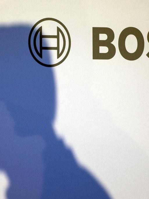 Der Schatten des Vorsitzenden von Bosch, Volkmar Denner, auf einer weißen Wand mit Bosch-Logo.