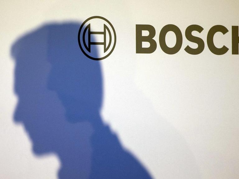 Der Schatten des Vorsitzenden von Bosch, Volkmar Denner, auf einer weißen Wand mit Bosch-Logo.
