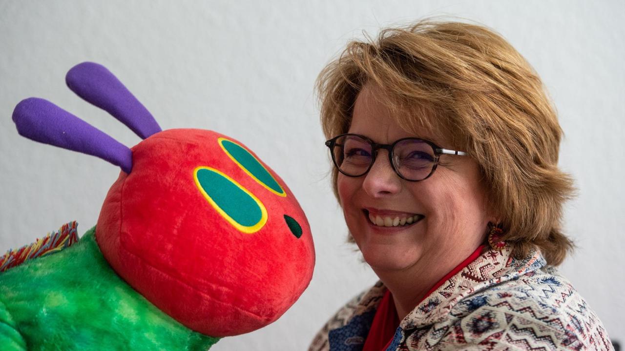 Daniela Filthaut vom Gerstenberg-Verlag lacht mit Brille und Wuschelfrisur in die Kamera. Vor sich hat sie eine Stoffraupe. Daniela Filthaut vom Gerstenberg-Verlag lacht mit Brille und Wuschelfrisur in die Kamera. Vor sich hat sie eine Stoffraupe.