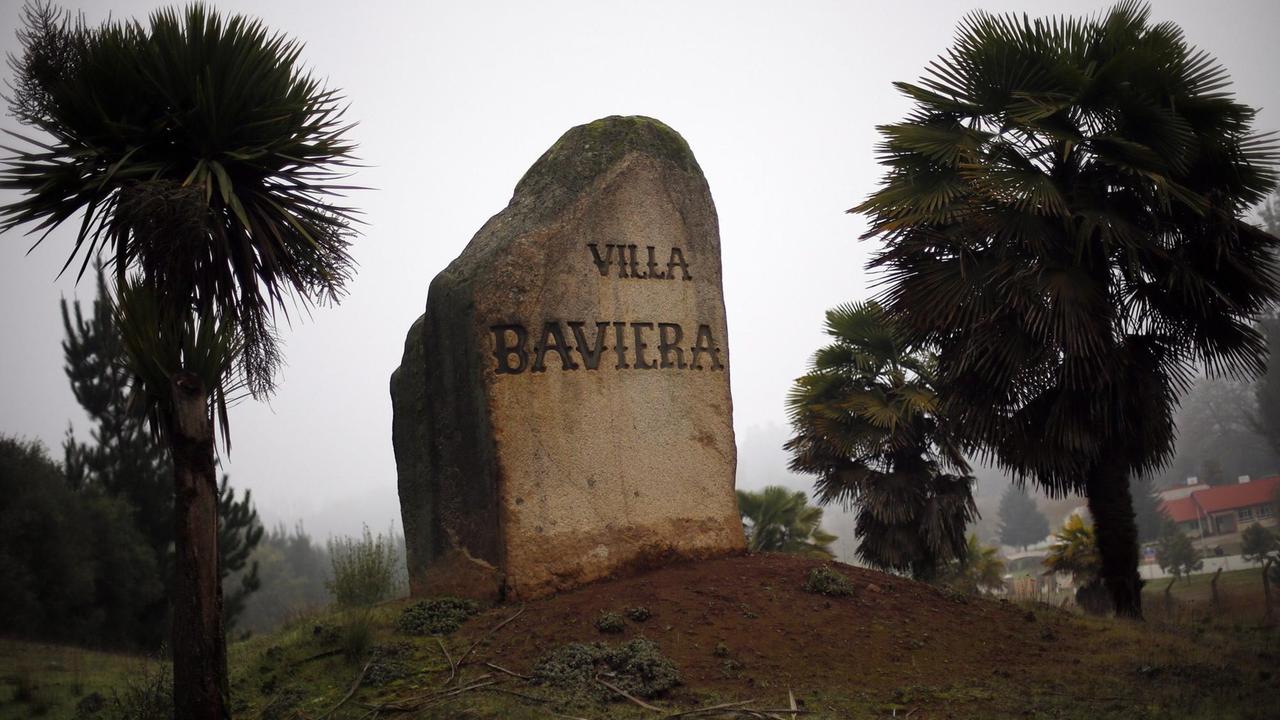 "Villa Bavaria" ist auf einem Stein zu lesen, der zwischen Palmen auf einem kleinen Hügel steht. Aufnahme von 2016.
