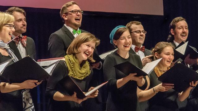Das Bild zeigt eine Nahaufnahme des Landesjugendchors Sachsen-Anhalt bei einem Auftritt während des Upgrade-Festivals. Alle Chormitglieder haben Noten in der Hand und ein Lächeln auf den Lippen.