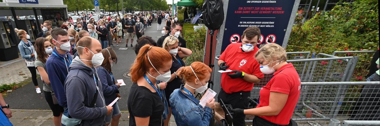 Am Einlass steht eine lange Schlange von Teilnehmerinnen und Teilnehmern mit Schutzmasken. Am Einlass steht eine lange Schlange von Teilnehmerinnen und Teilnehmern mit Schutzmasken.