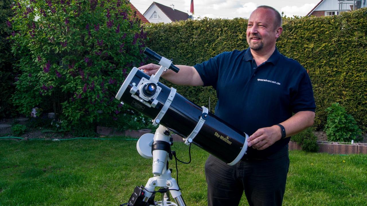 Amateurastronom Thomas Wehr steht hinter seinem Teleskop im Garten. Hinter ihm ist eine sauber geschnittene Hecke und dahinter Einfamilienhäuser. Amateurastronom Thomas Wehr steht hinter seinem Teleskop im Garten. Hinter ihm ist eine sauber geschnittene Hecke und dahinter Einfamilienhäuser.