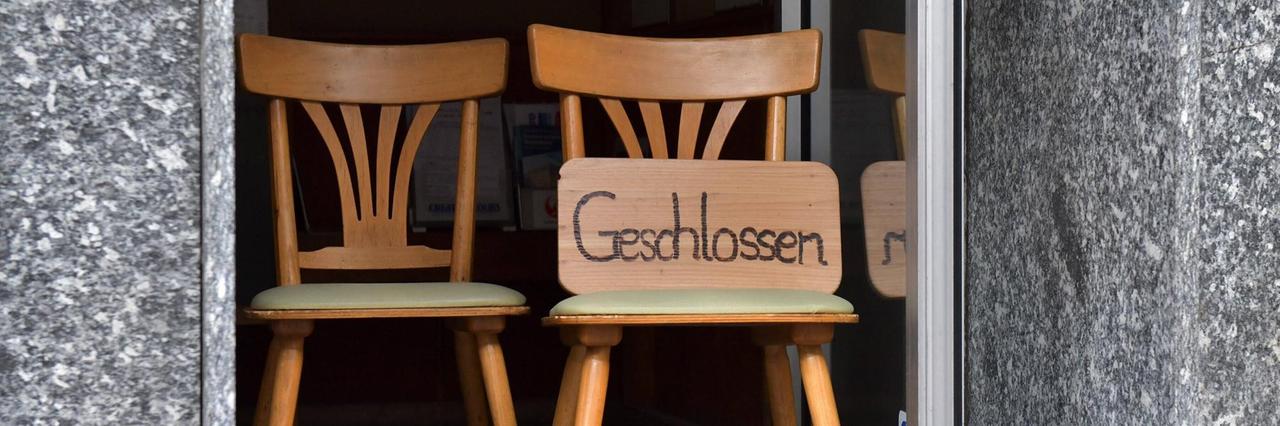 "Geschlossen" steht auf einem Schild, das im auf einem Stuhl im Türrahmen lehnt. "Geschlossen" steht auf einem Schild, das im auf einem Stuhl im Türrahmen lehnt.